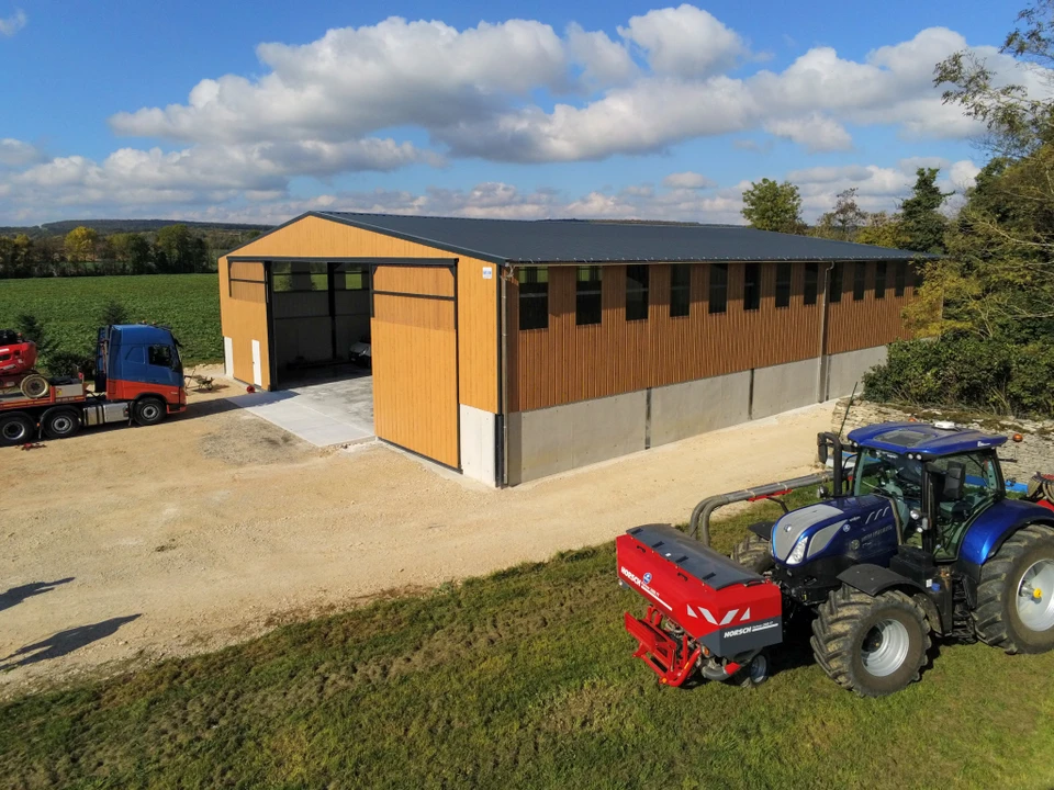 Chantier de construction extérieur avec une charpente métallique en cours d'assemblage, montrant des profilés d'acier et des structures métalliques en place. On voit des ouvriers en tenue de chantier et équipement de sécurité travaillant à la mise en place des éléments métalliques, avec des liaisons boulonnées visibles. L'image doit montrer clairement un travail de construction métallique professionnel et de qualité.